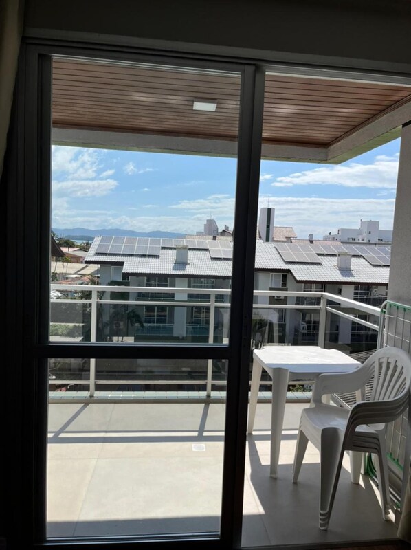 A balcony with a view of solar panels on neighboring buildings, a white table, and two white chairs.