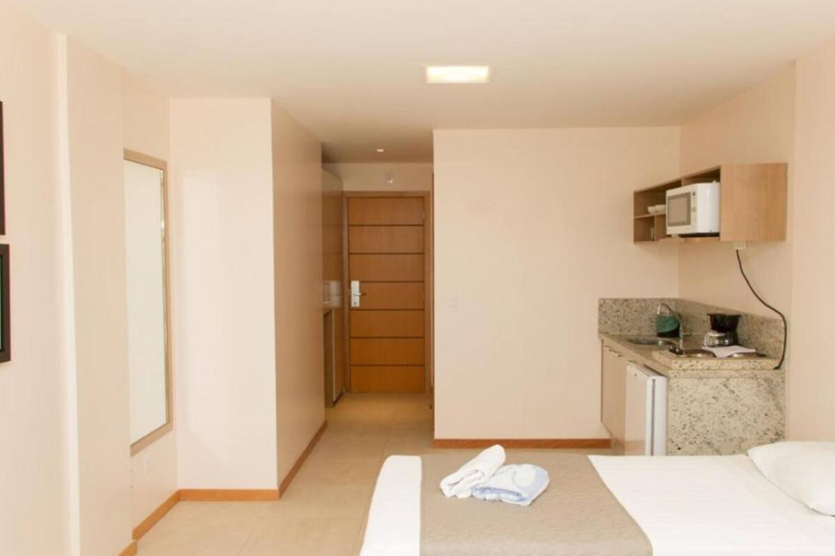 Habitación de hotel con cama, kitchenette pequeño, puerta que da a un baño y un espejo en la pared.