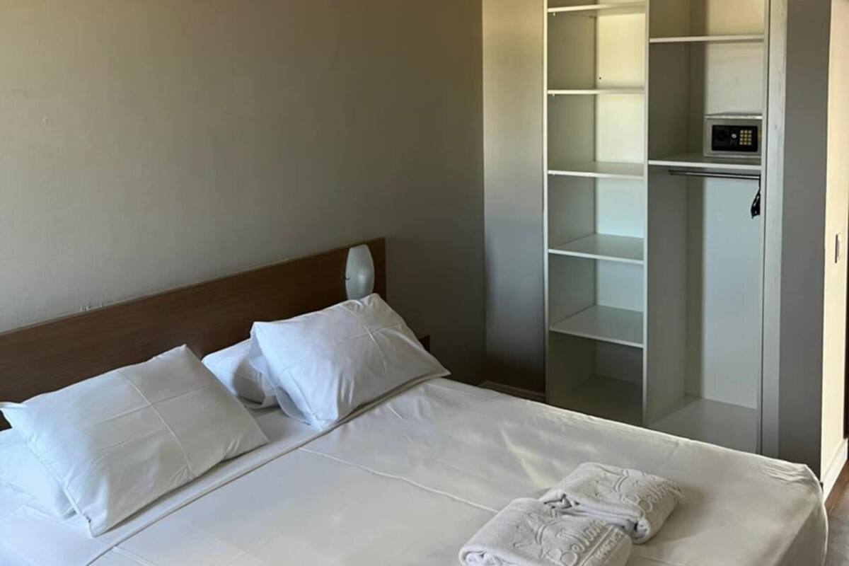Una habitación de hotel con una cama bien hecha, un armario y un panel de control en la pared.