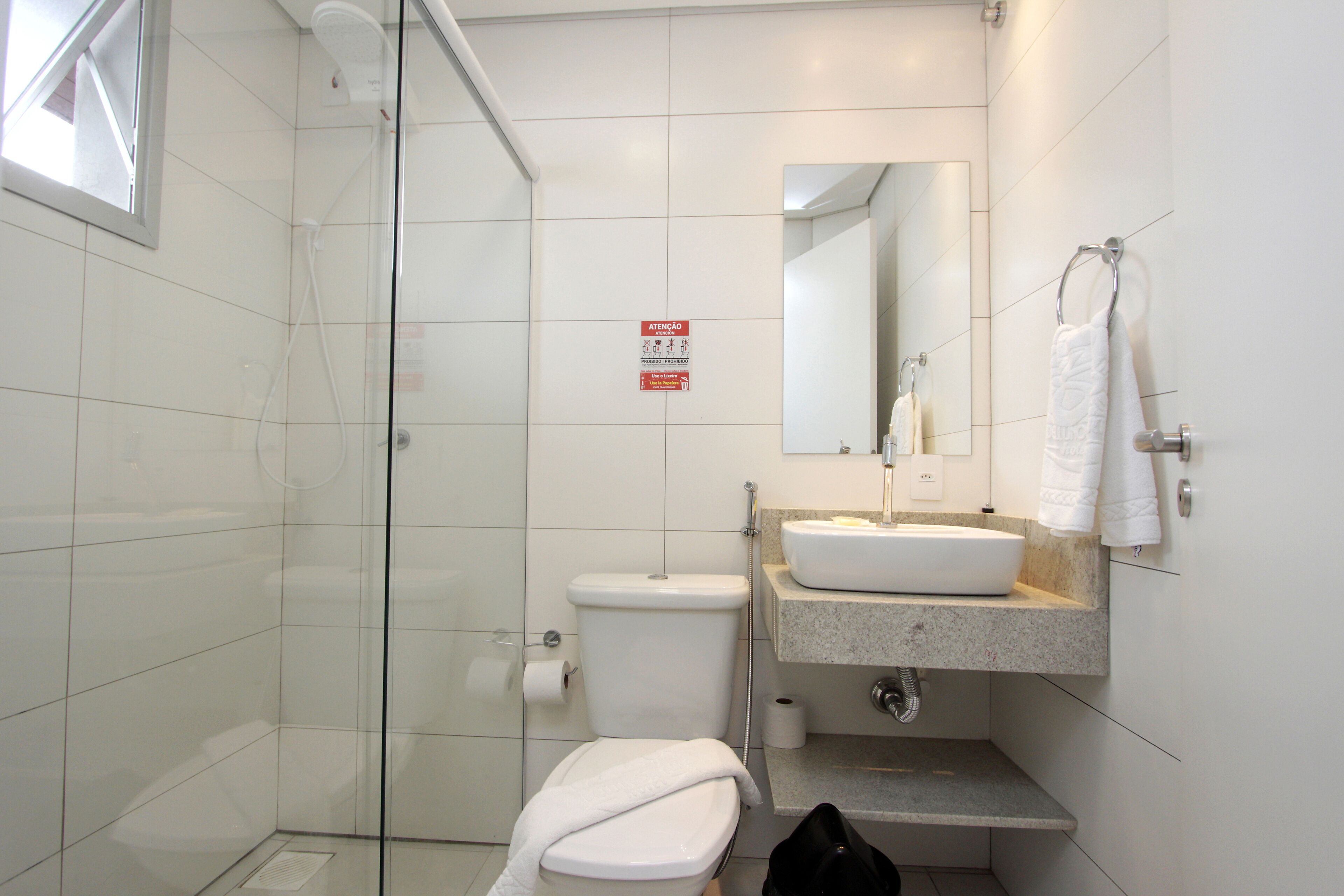 Un baño moderno con cabina de ducha de vidrio, inodoro, lavamanos con espejo y toallero.