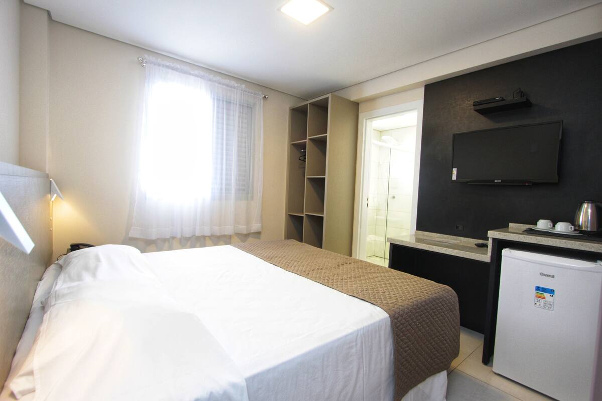 Habitación de hotel con cama, escritorio con computadora, refrigerador y televisor montado en la pared.
