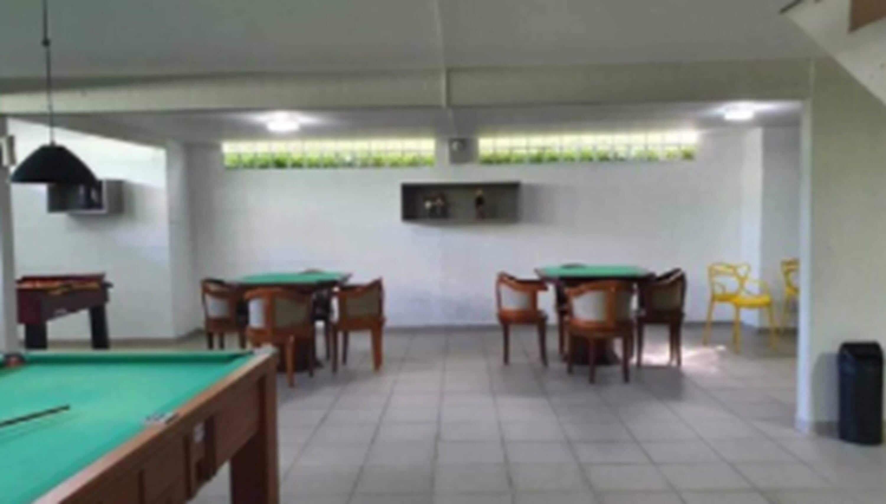 Una habitación con mesa de billar, cuatro mesas de madera con sillas, un televisor montado en la pared y una ventana con persianas.