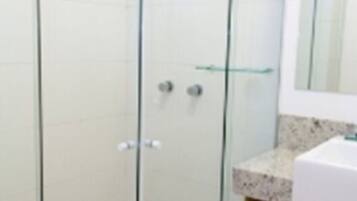 Un baño moderno con ducha envuelta en vidrio, un lavamanos blanco y un espejo sobre él.