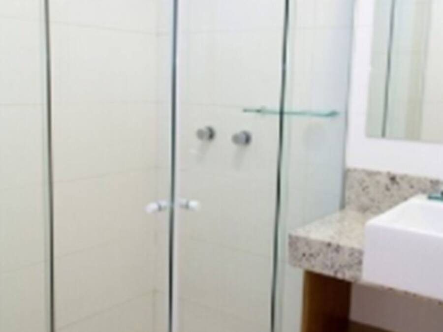 Un baño moderno con ducha envuelta en vidrio, un lavamanos blanco y un espejo sobre él.