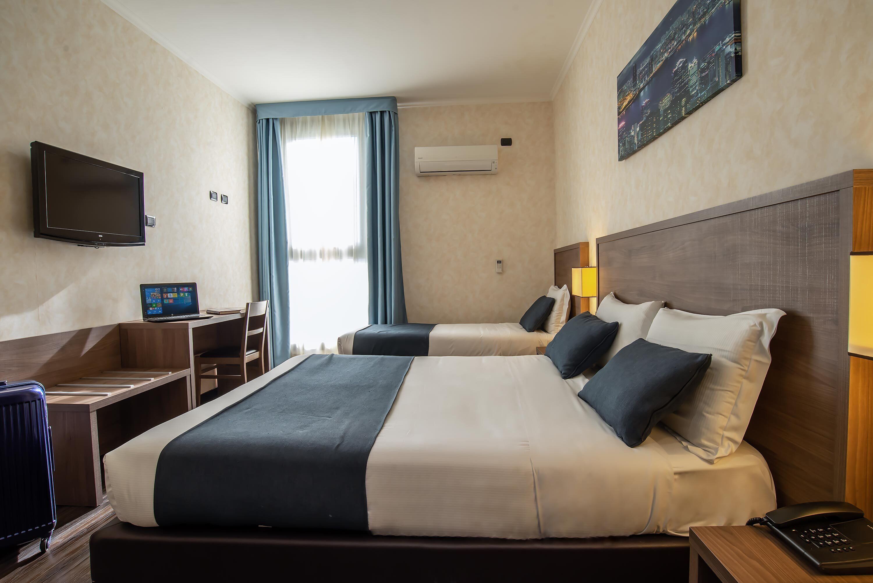 Habitación de hotel con una cama grande, un escritorio, una computadora portátil, un televisor y aire acondicionado.