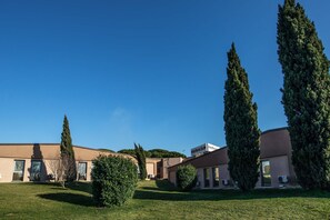 A hotel with a modern design, featuring a flat roof and a well-maintained lawn with tall cypress trees. - Hotel Roma Sud (Frascati)