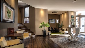 A modern living room with a staircase, a large potted plant, and a sofa. - Hotel Roma Sud (Frascati)