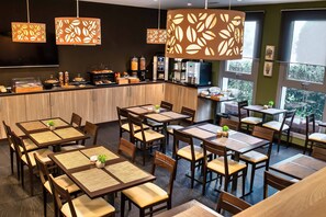 A restaurant with multiple tables and chairs, a counter with food items, and hanging decorative lights.