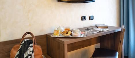 A hotel room with a wooden desk, a television mounted on the wall, a brown leather bag, and a chair.