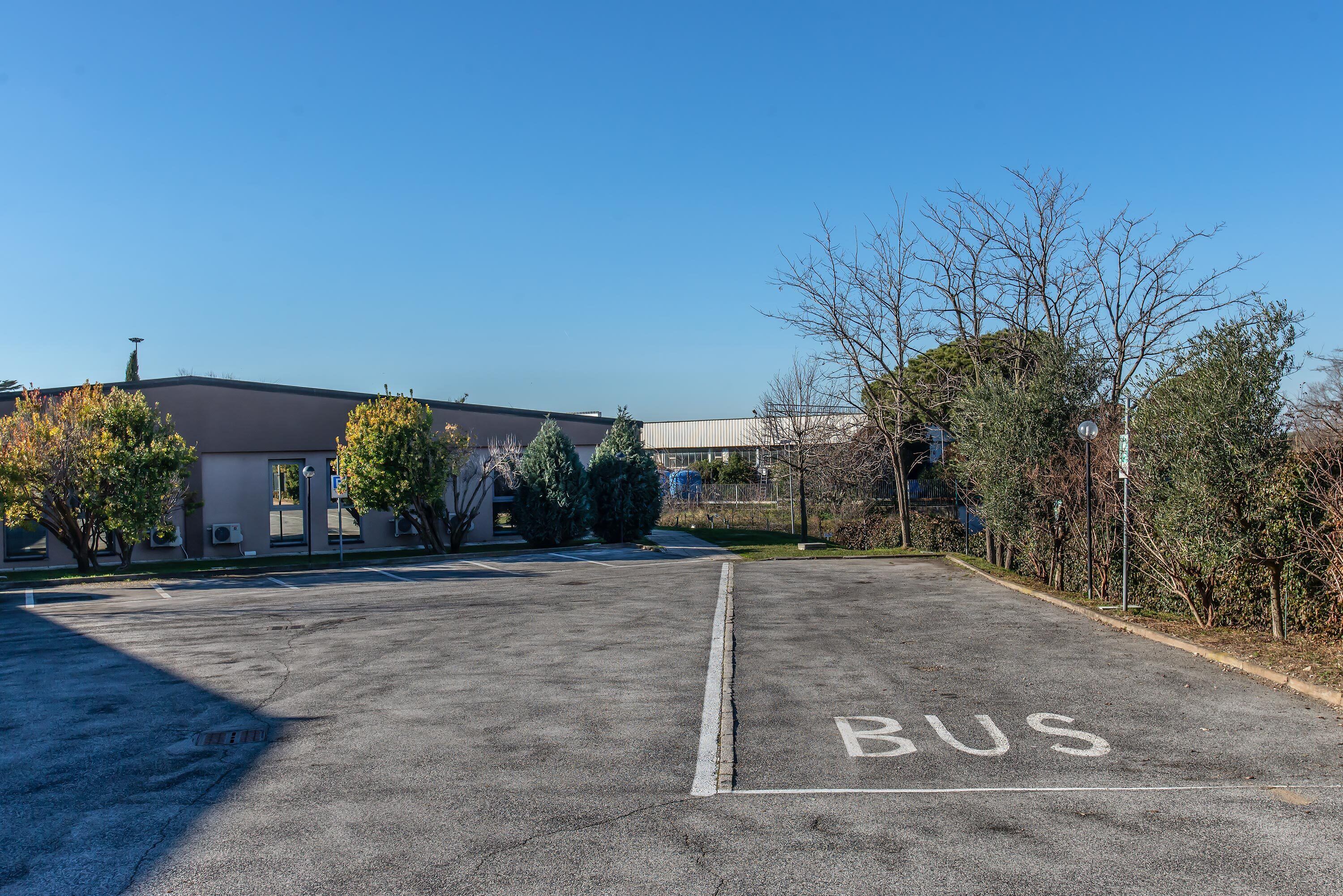 A parking lot with a 'BUS' sign, a building with a flat roof, and some trees.