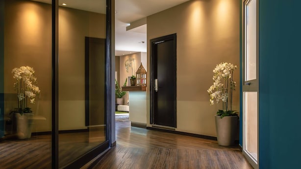 A hallway with wooden flooring, a glass partition, and two potted white orchids. - Hotel Roma Sud (Frascati)