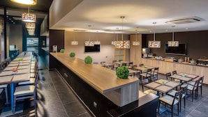 A modern restaurant with a long counter, multiple tables, and hanging pendant lights. - Hotel Roma Sud (Frascati)