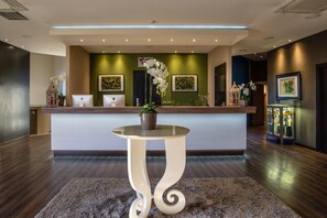 A reception area with a counter, two computers, a potted plant, and framed artwork on the walls. - Hotel Roma Sud (Frascati)