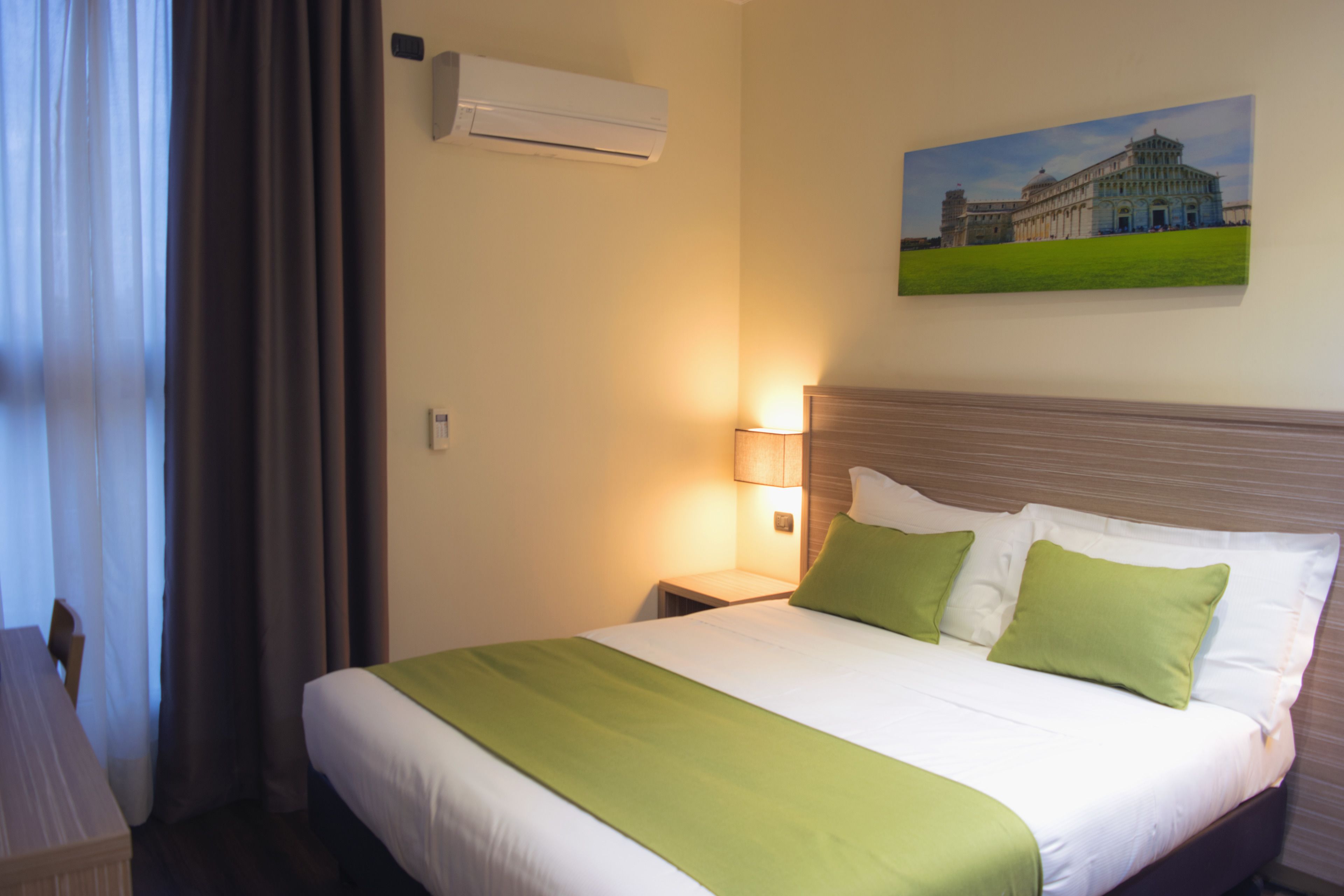 Une chambre d’hôtel avec un lit, une table de chevet, une lampe, un appareil de climatisation et un tableau au mur.
