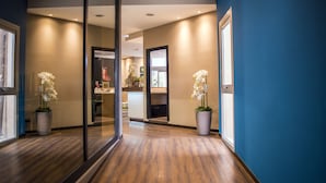 A modern hotel corridor with wooden flooring, blue walls, and potted white orchids. - Hotel Roma Sud (Frascati)