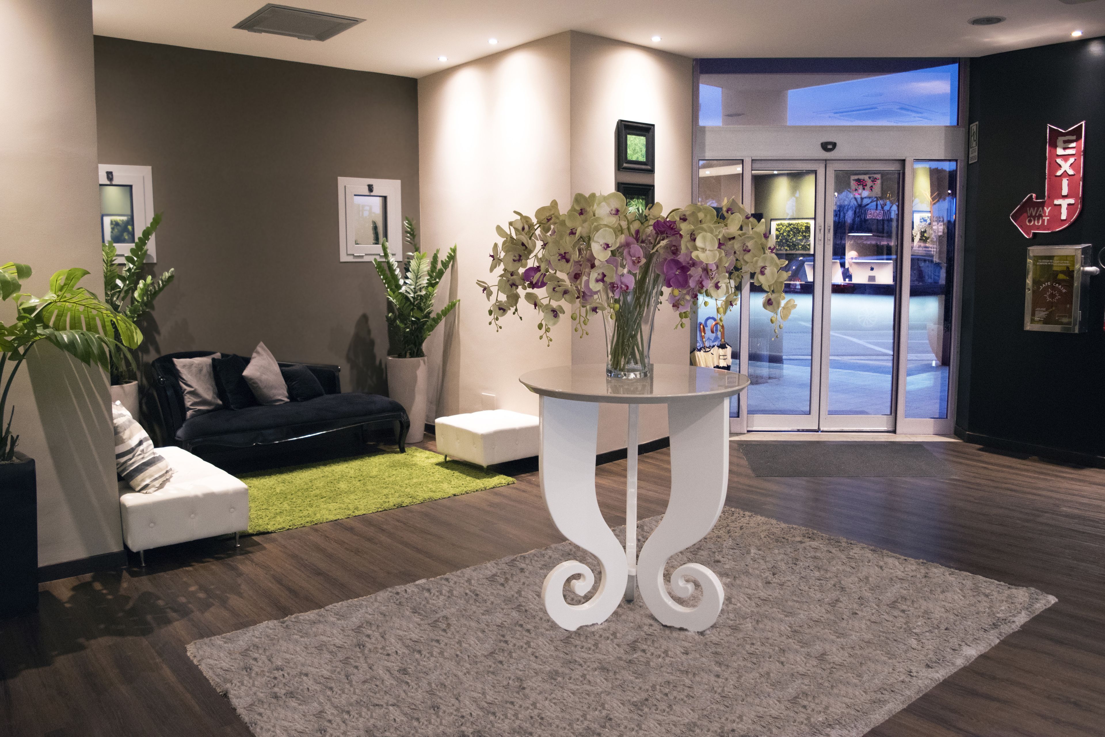 A modern lobby with a white sofa, a round table with a vase of flowers, and a green rug.
