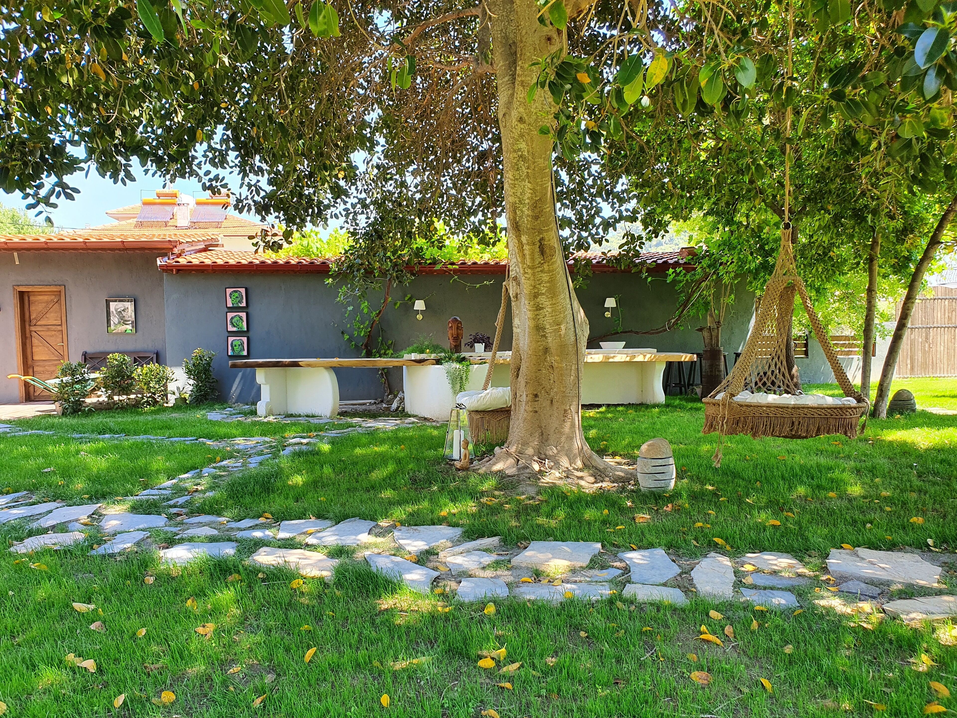 A house with a stone pathway leading to a wooden deck, surrounded by greenery and a tree.