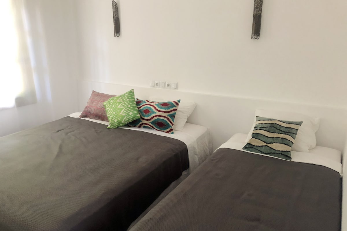 A hotel room with two beds, each with a dark-colored bedspread and multiple patterned pillows.