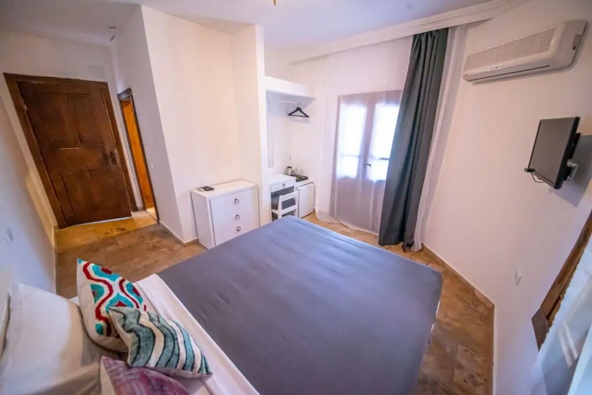 Un dormitorio con cama, mesita de noche, armario, espejo, lámpara colgante y ventana con cortinas.