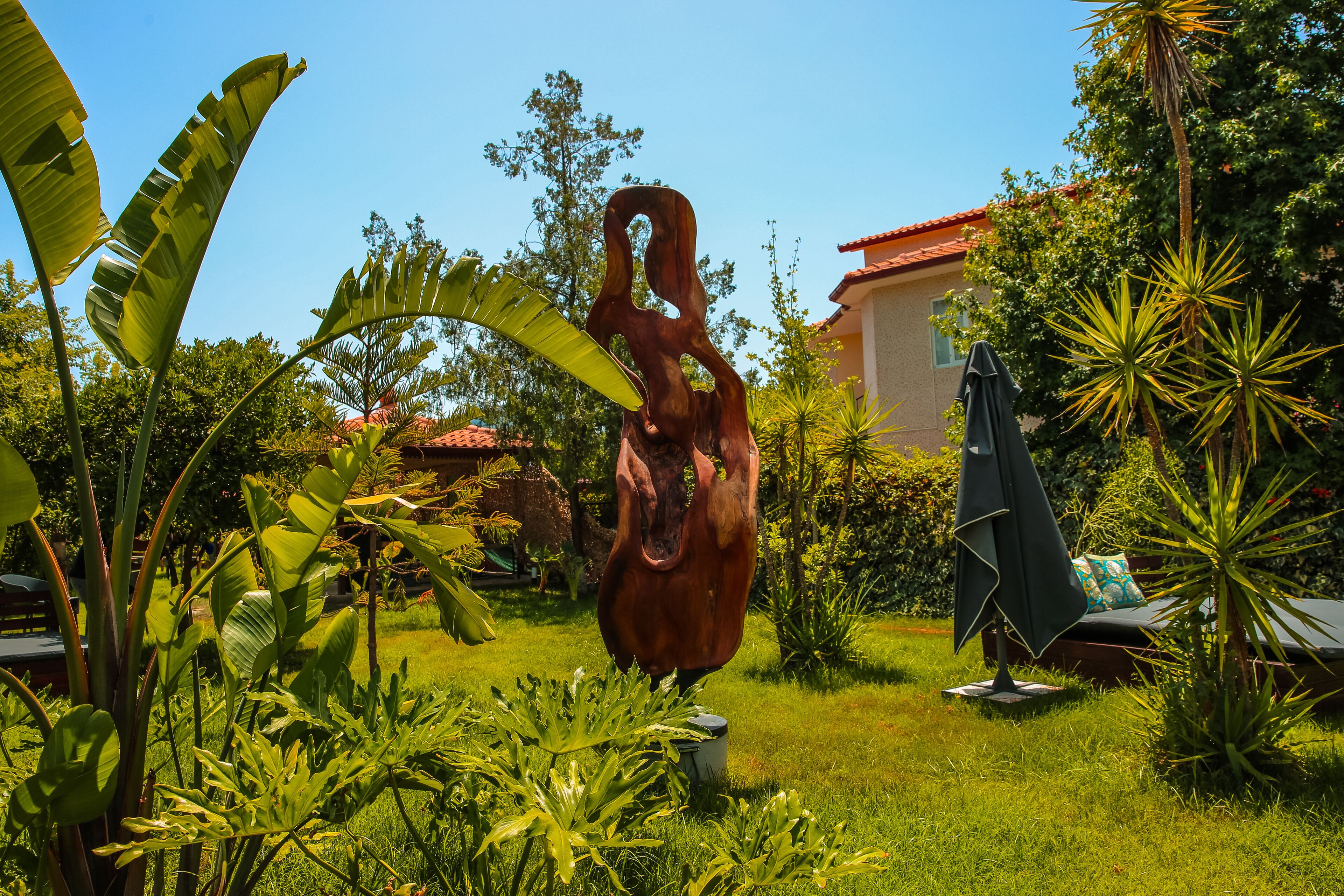 A garden with a large sculpture, lush greenery, and a building with a red roof.