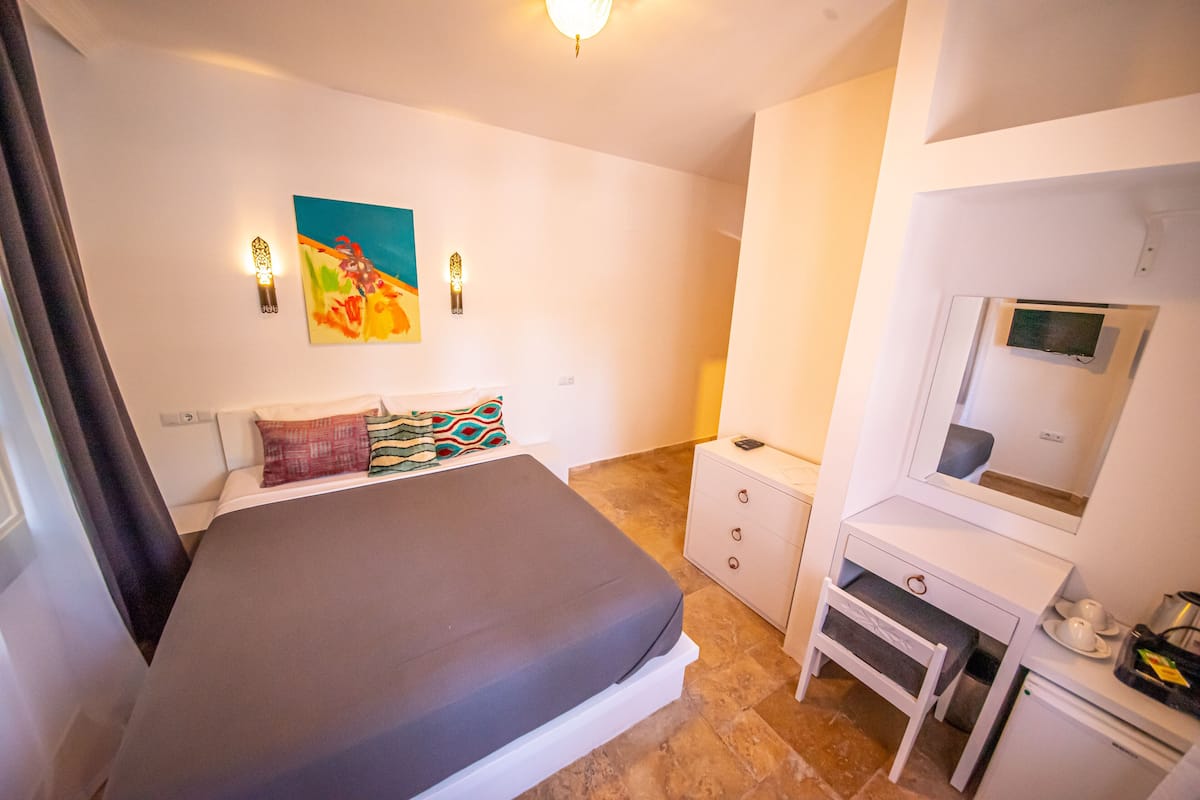 A bedroom with a bed, bedside table, dresser, and a painting on the wall.
