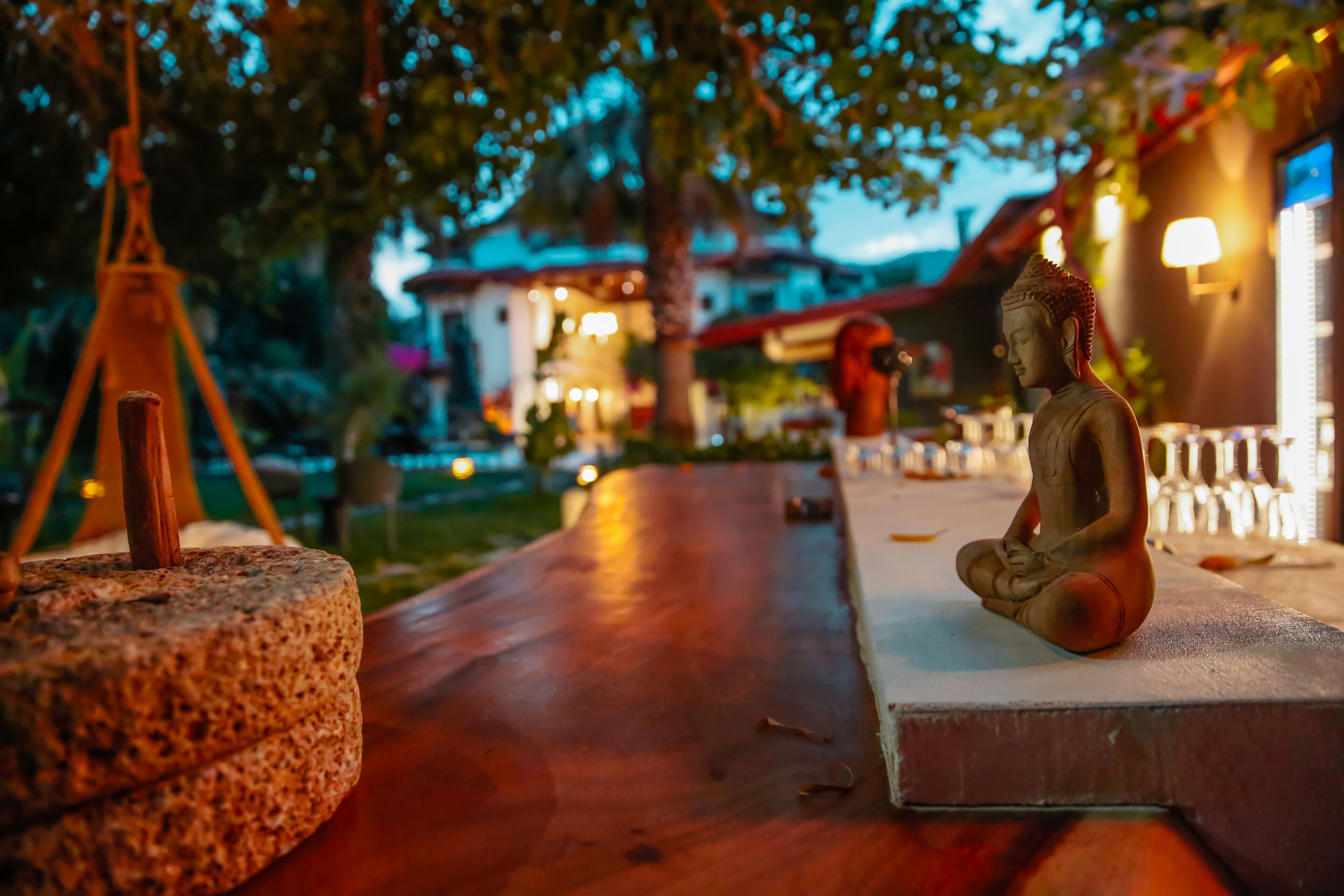 Una estatua de Buda sobre un pedestal con una mesa de madera y una base de lámpara de piedra en un jardín.
