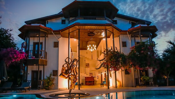 A large, multi-story building with a covered outdoor area, a swimming pool, and a central sculpture. - Murat Paşa Konağı Boutique Hotel (Ortaca)