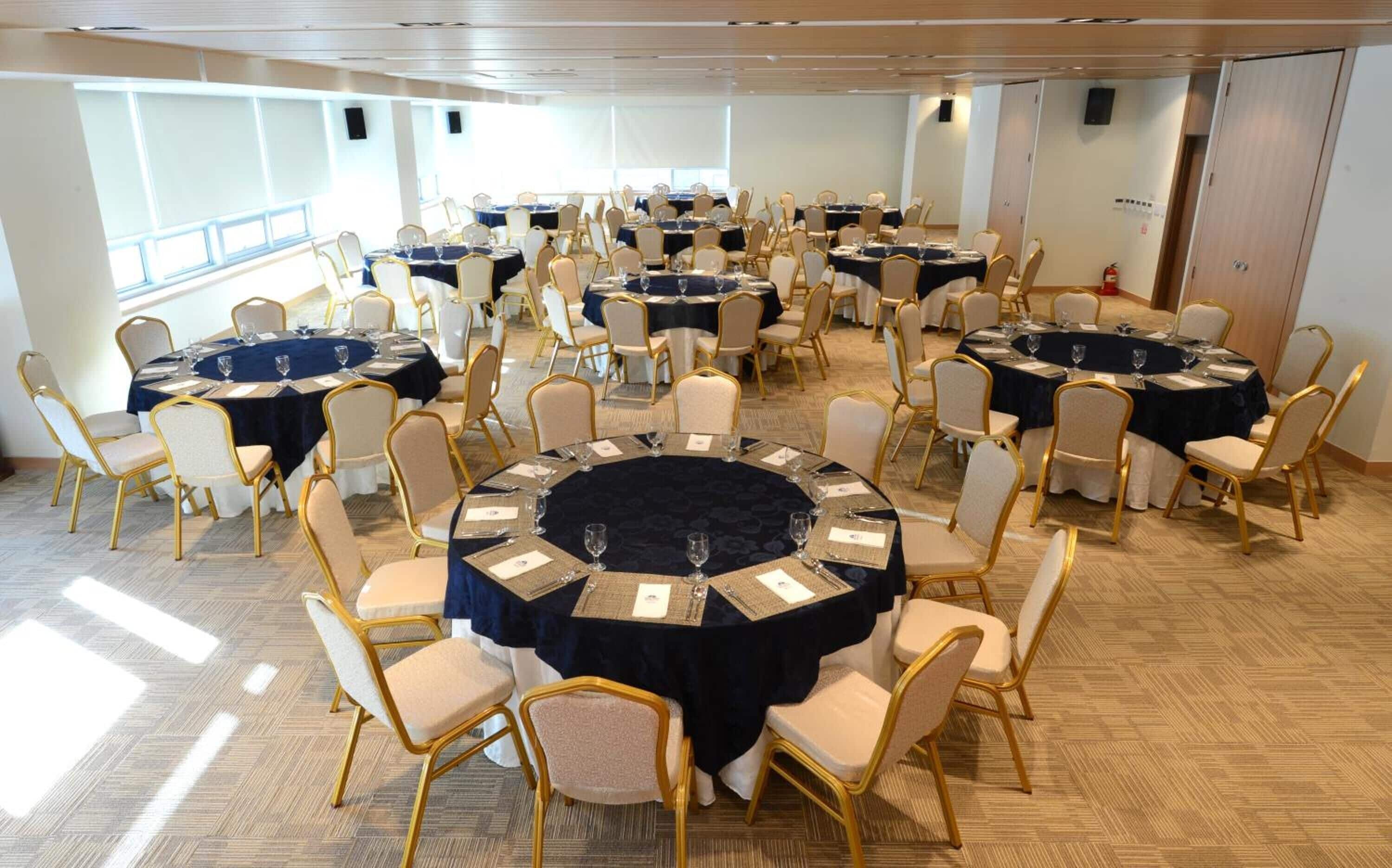 A conference room with multiple round tables, each set with chairs and tablecloths.