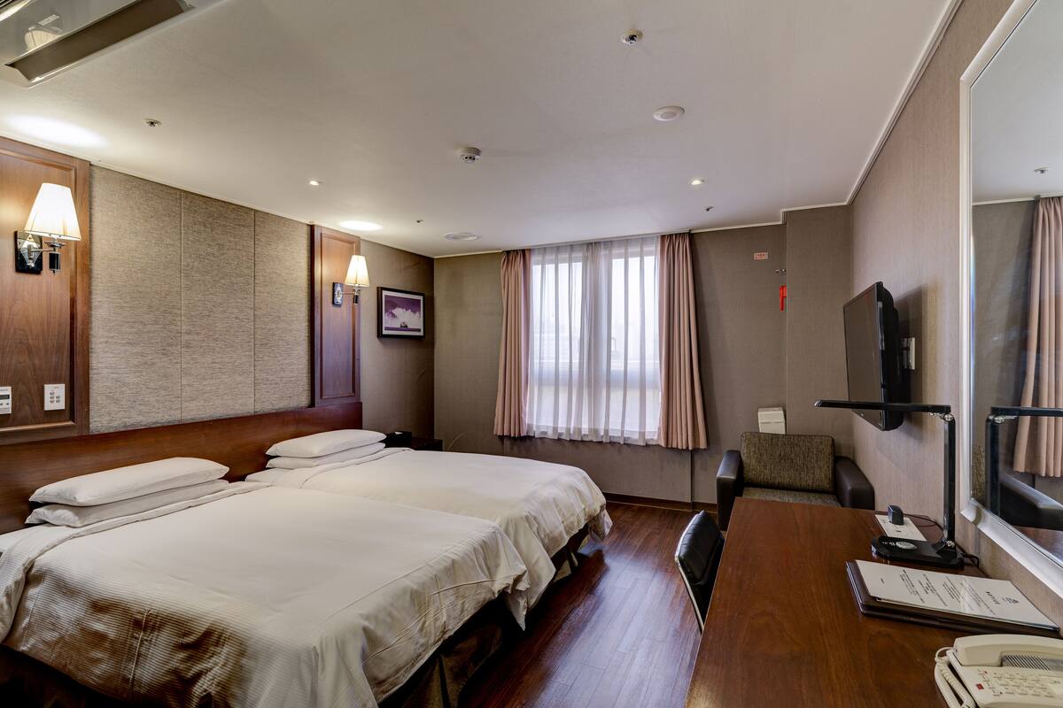 Habitación de hotel con dos camas, un escritorio, una silla, un televisor y una ventana con cortinas.