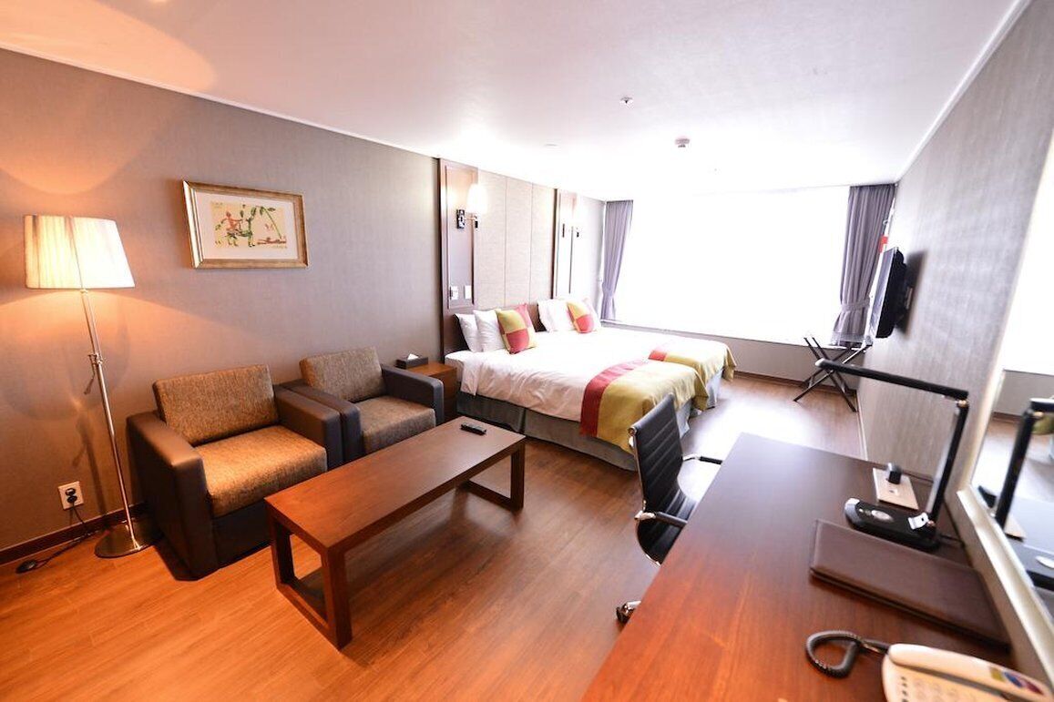 A hotel room with a bed, a sofa, a desk, a lamp, and a television.