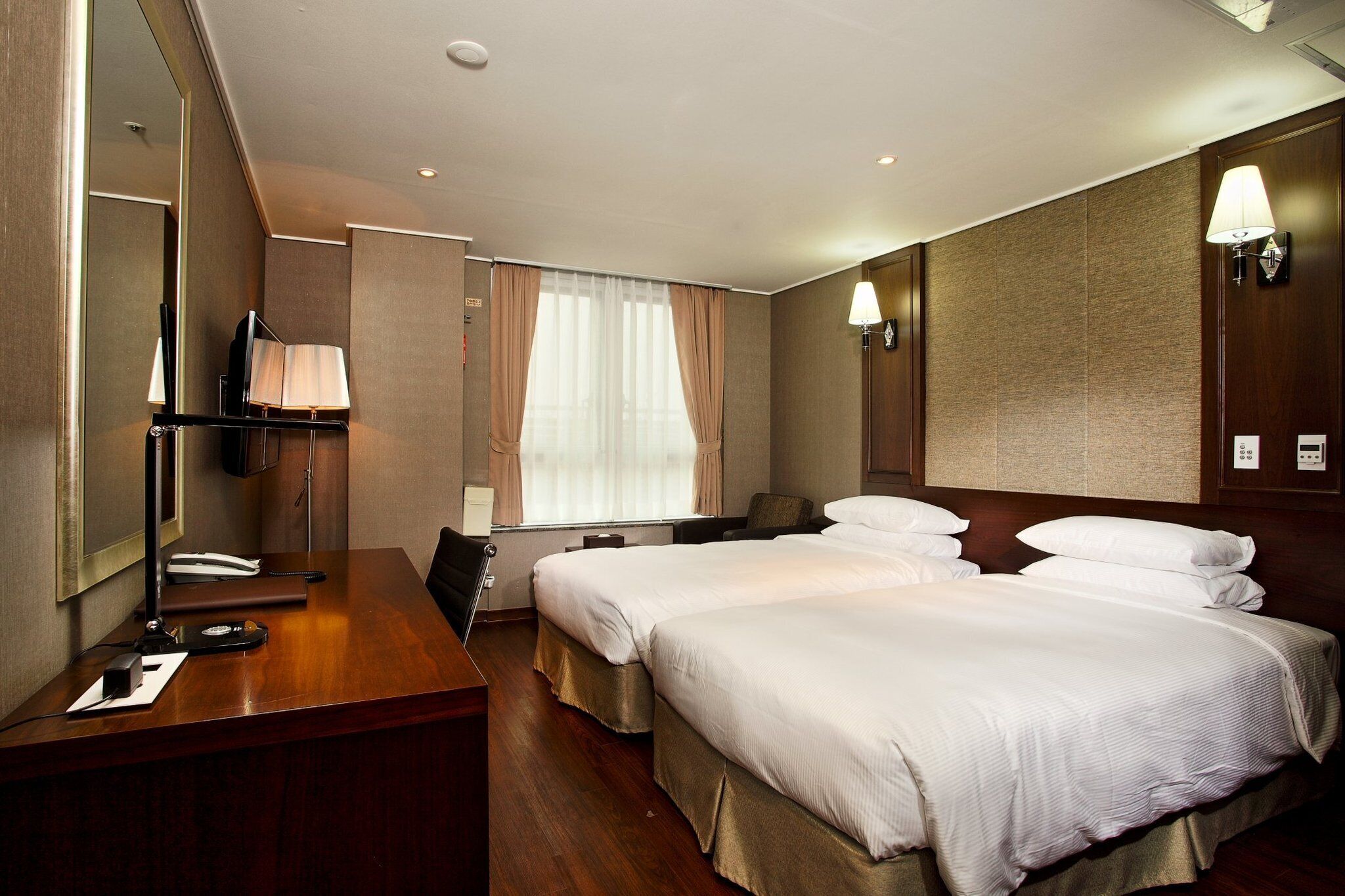 A hotel room with two beds, a desk with a telephone, and a large mirror.
