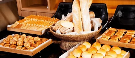 A buffet table with various baked goods including bread, croissants, and rolls.