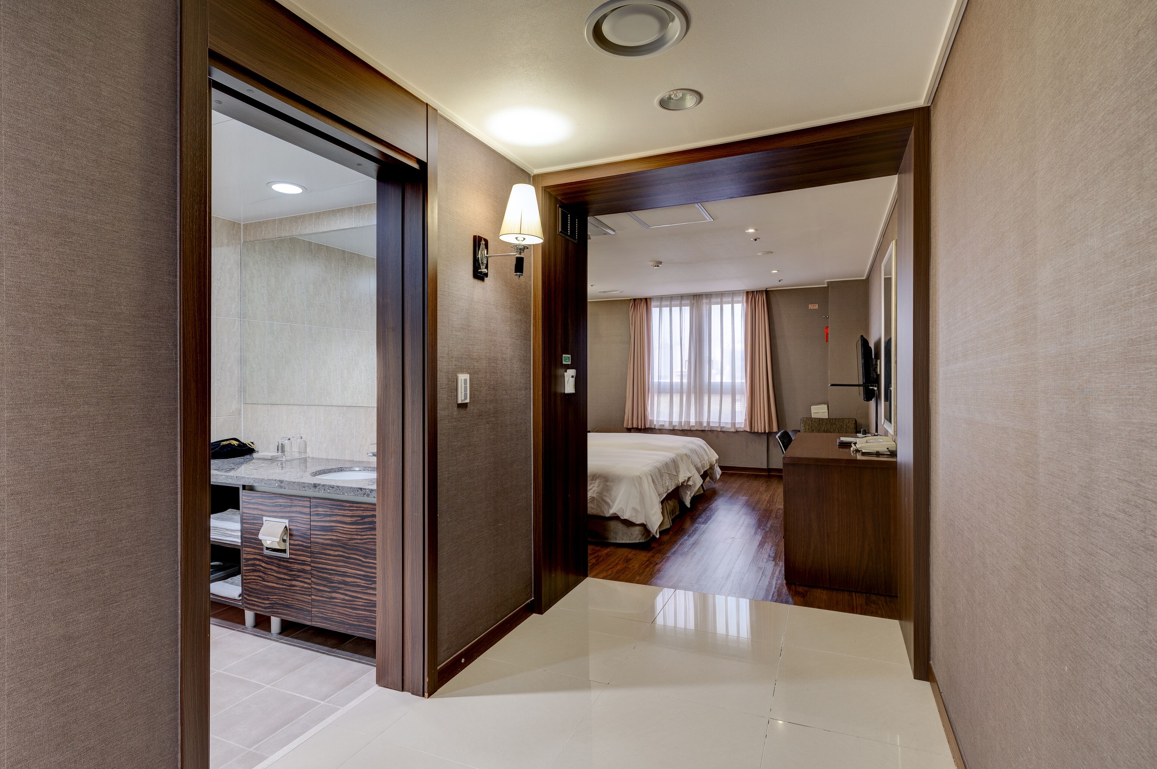 A hotel room with a bathroom, a bed, a desk, and a TV.