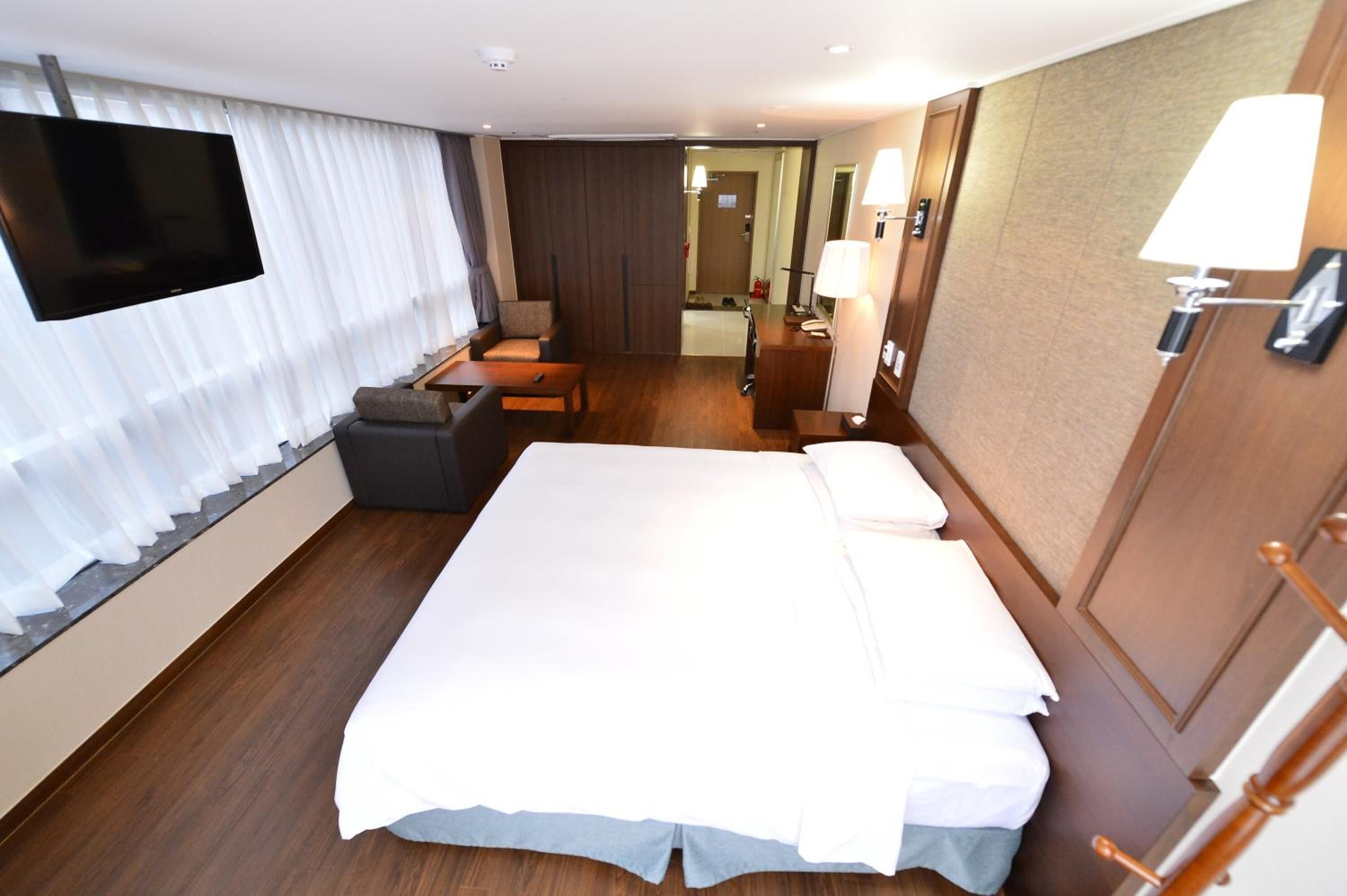 Une chambre d’hôtel avec un grand lit, un bureau, une chaise, une télévision et une salle de bain visible à travers une porte.