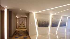 Un pasillo moderno de hotel con alfombra estampada, iluminación empotrada y arte abstracto en las paredes.
