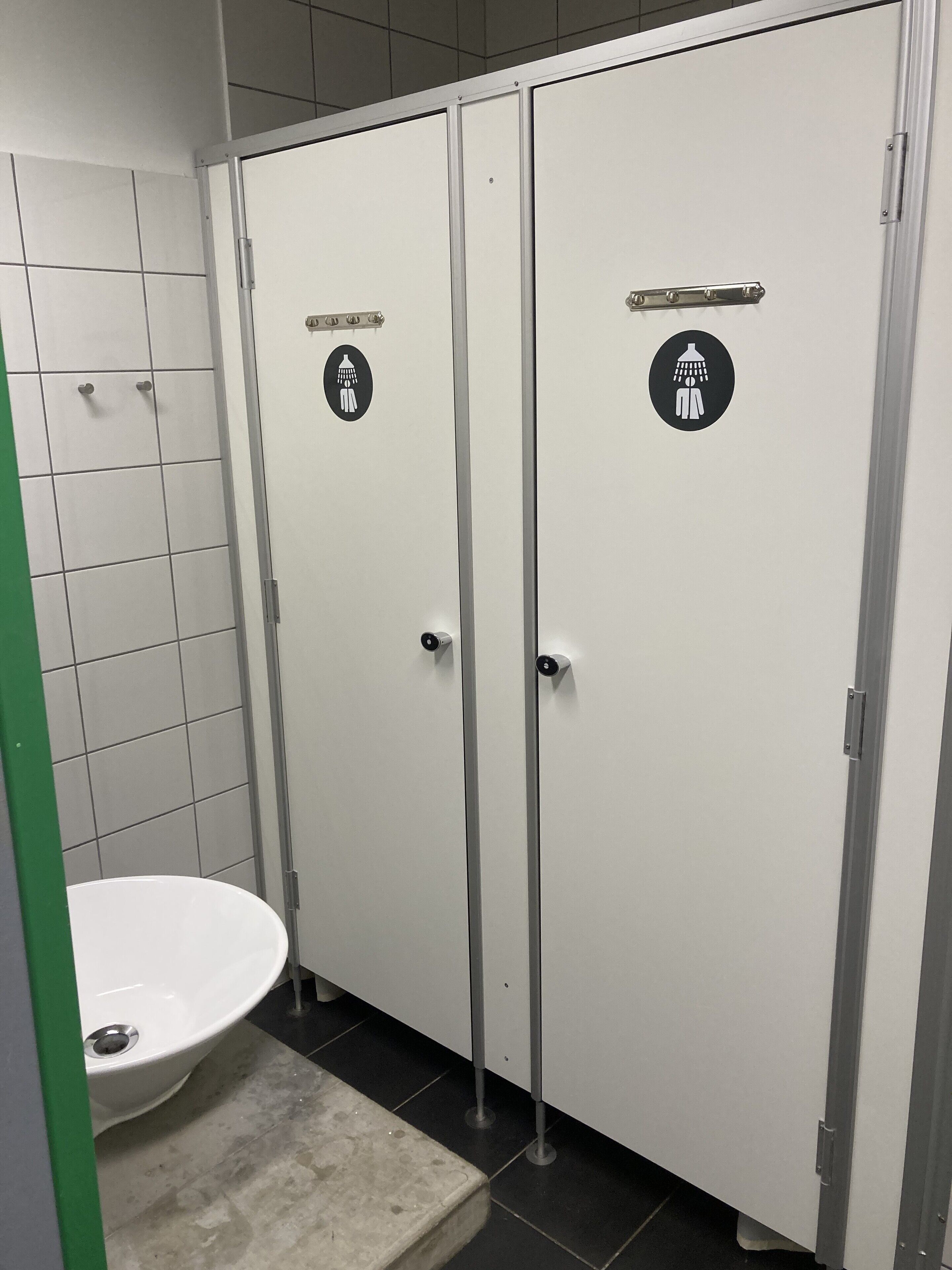 Un baño de hombres con dos puertas, cada una señalizada con un icono de ducha, un inodoro y un secador de manos.