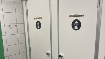 Un baño de hombres con dos puertas, cada una señalizada con un icono de ducha, un inodoro y un secador de manos.