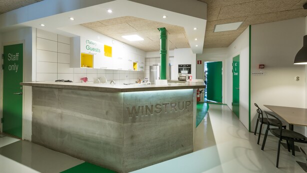 En modern inredning med en central köksö märkt "WINSTRUP", gröna dörrar och en stilren, minimalistisk design.