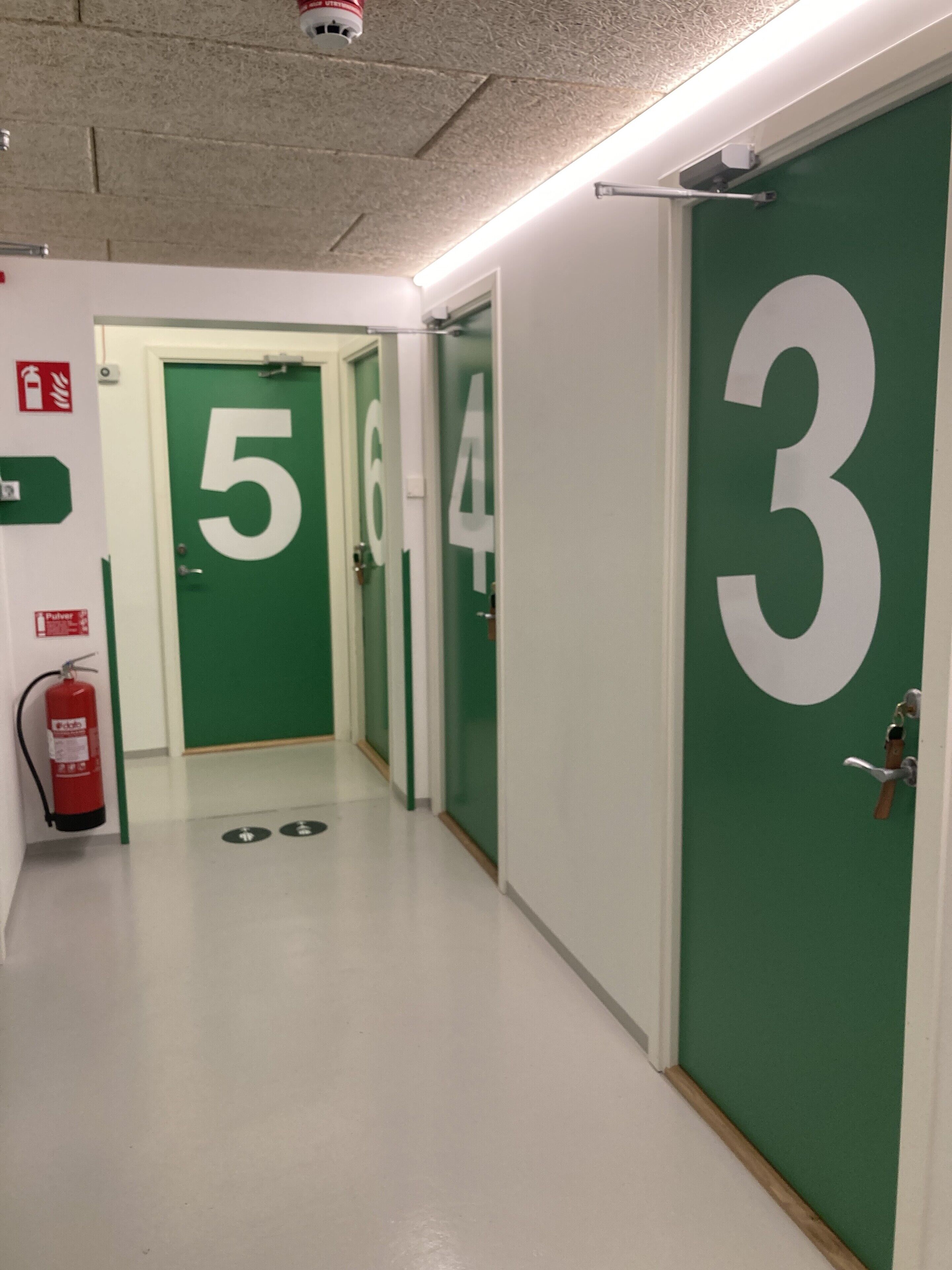 Un pasillo con puertas verdes numeradas 3, 4, 5 y 6.