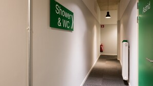 En hall med en skylt som visar vägen till duschen och toaletten, en brandsläckare och en grön dörr med namnet "Astrid" på.