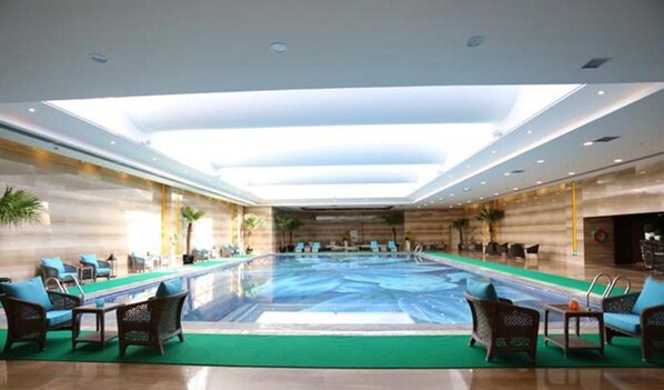 Una piscina interior amplia con diseño moderno, rodeada de sillones de descanso y un techo alto con tragaluces.