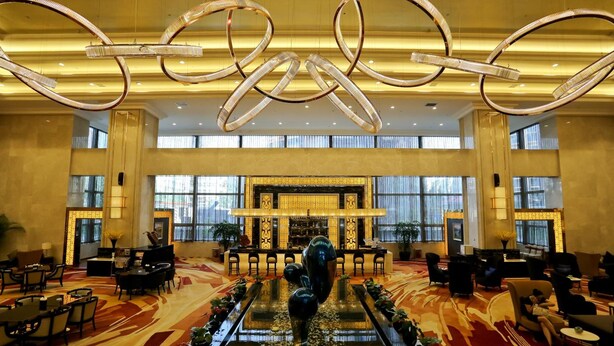 Een ruime lobby met een centraal gelegen receptiebalie, zithoeken en een decoratieve fontein.