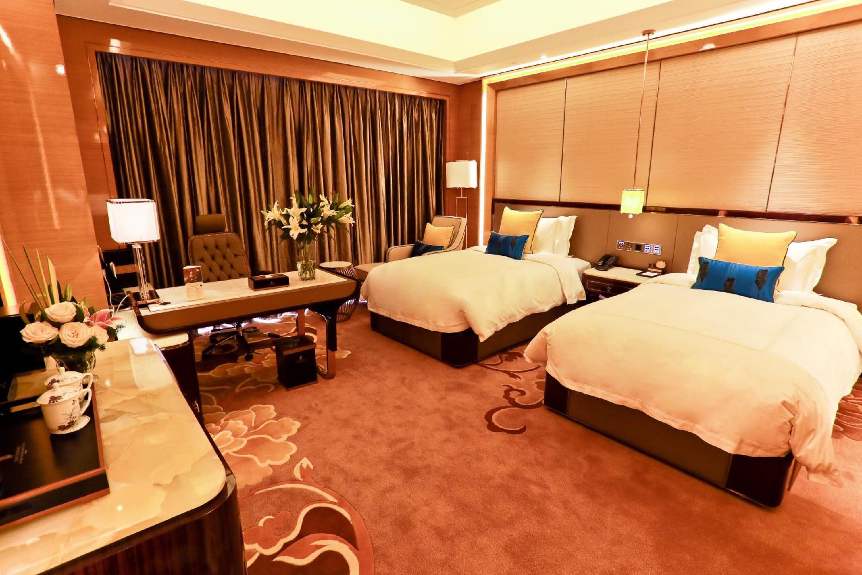 A hotel room with two beds, a desk, a chair, a small table, and a curtain.