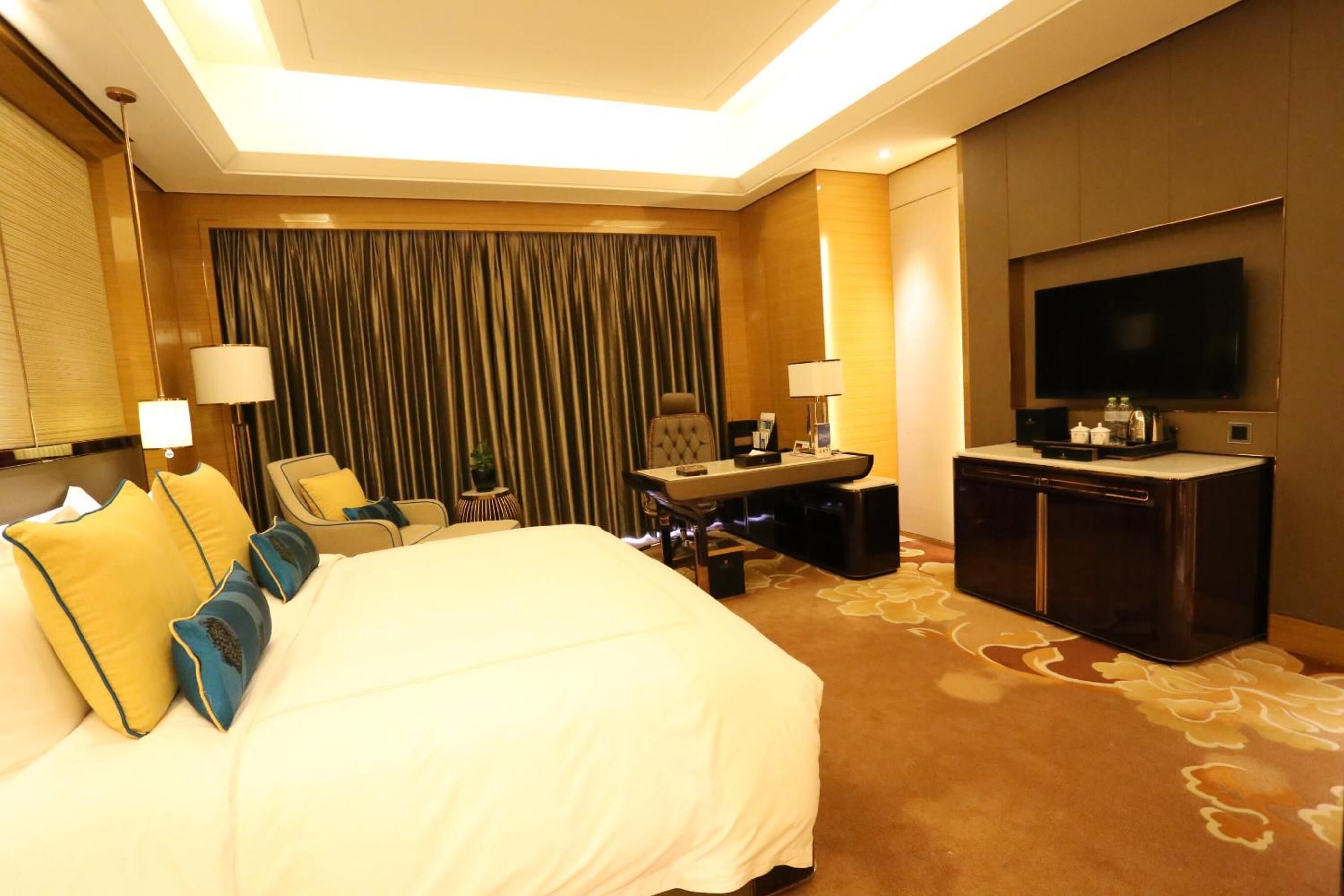 A hotel room with a large bed, a desk, a television, and a seating area.
