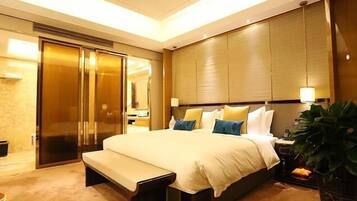 A hotel room with a large bed, a bench, a wardrobe, and a potted plant.