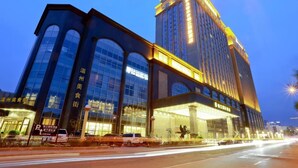Een modern hotel met een opvallende glazen gevel en een hoog gebouw met verlichte reclameborden.
