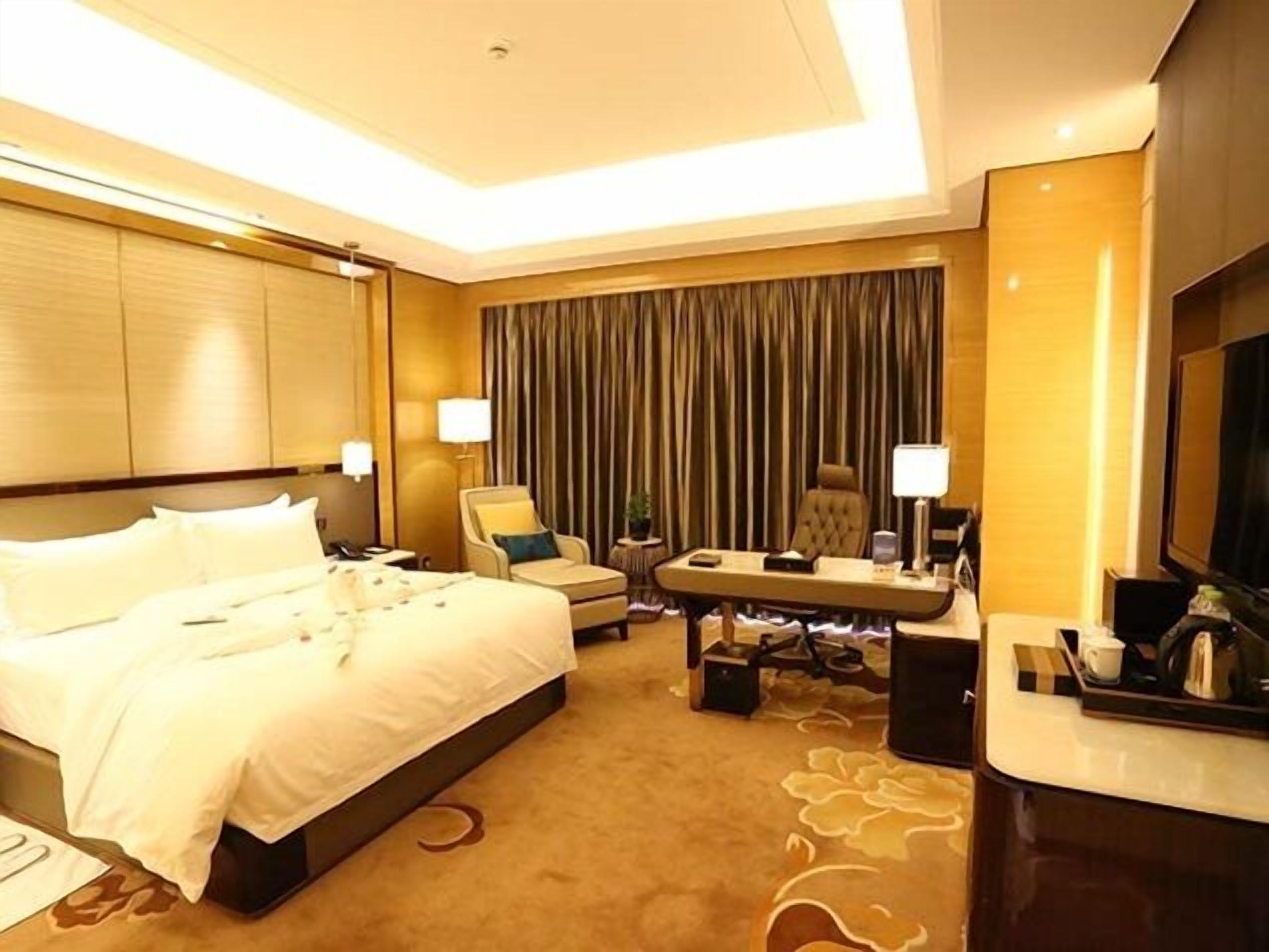 Ein Hotelzimmer mit einem großen Bett, einem Schreibtisch mit Stuhl, einem Fernseher und einem Vorhang im Hintergrund.