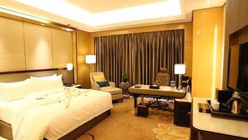 Ein Hotelzimmer mit einem großen Bett, einem Schreibtisch mit Stuhl, einem Fernseher und einem Vorhang im Hintergrund.