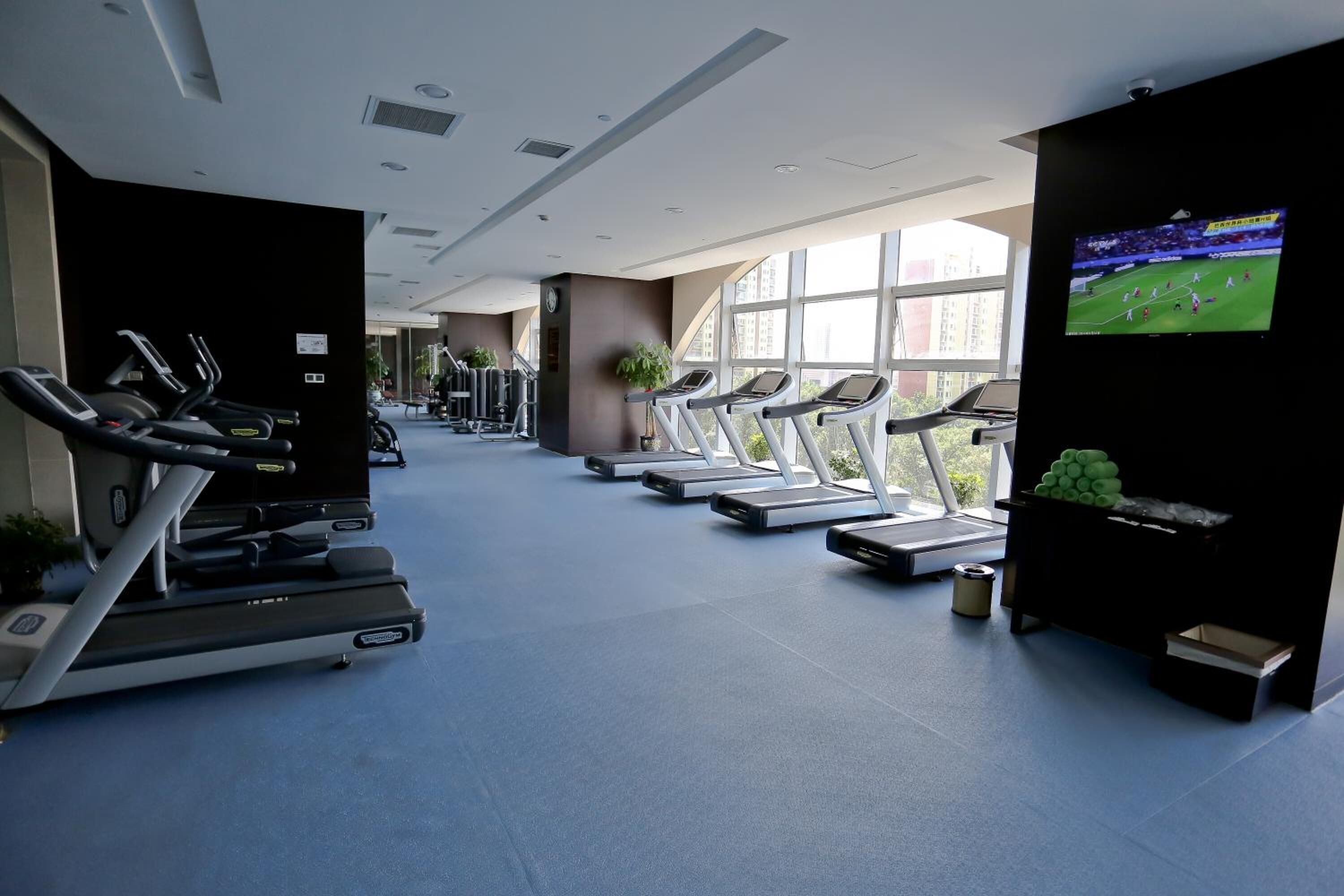A gym with treadmills, exercise machines, and a TV screen displaying a sports event.