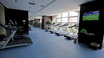 A gym with treadmills, exercise machines, and a TV screen displaying a sports event.